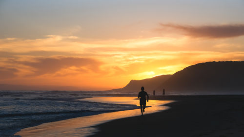 Silhouette people walking at beach against sky during sunset