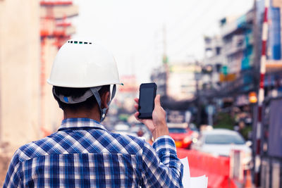 Rear view of man using mobile phone in city