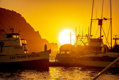 Sailboats moored at harbor against sky during sunset