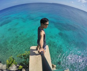 Fish-eye lens of young man with monopod standing on pier over sea