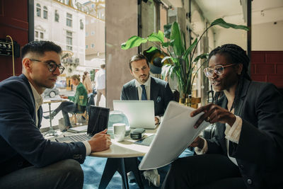 Young businesswoman discussing over document with male colleagues sitting in hotel lounge