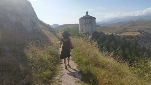 Rear view of woman walking on pathway by mountain