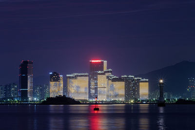 Illuminated city by sea against sky at night