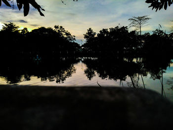 Silhouette trees by lake against sky during sunset