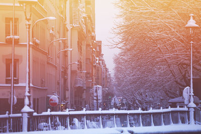 Snow covered street by buildings in city