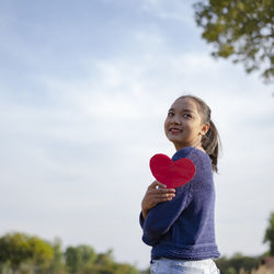 Portrait of woman holding heart shape against sky