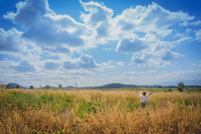 Rear view of young woman standing on grassy field against cloudy sky