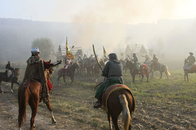 Rear view of people riding horses on field against sky