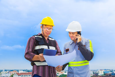 Engineer with colleague holding blueprint against sky