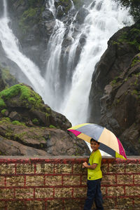 Rear view of man with umbrella walking on rock