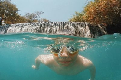 Boy swimming in river with waterfall in background