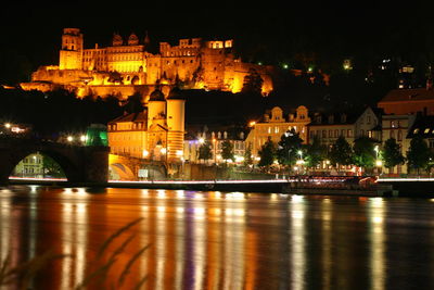 Illuminated bridge over river by buildings in city at night