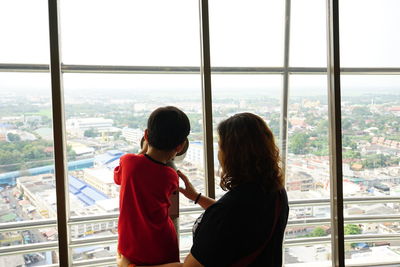 Rear view of boy with mother looking at cityscape through binocular