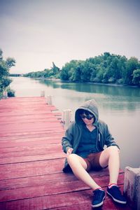 Man sitting on pier over lake against sky