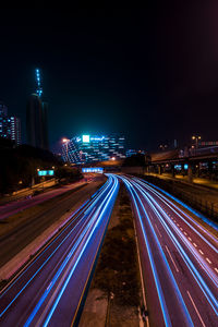 Light trails on road amidst illuminated buildings in city at night