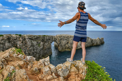 Woman standing on rock by sea against sky