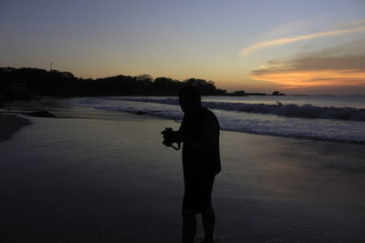 Silhouette man standing on beach against sky during sunset