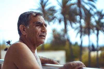 Shirtless senior man standing by railing at balcony