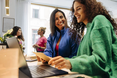 Happy businesswoman with smiling female colleague looking at laptop in office