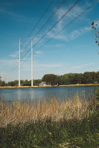 Electricity pylon by lake against sky