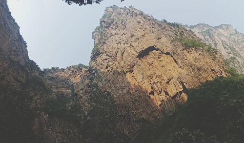 Low angle view of rocks and mountains against clear sky