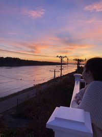 Woman holding umbrella by sea against sky during sunset