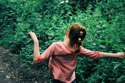 Rear view of girl with arms outstretched against plants