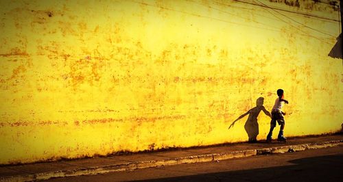 Full length of boy inline skating on footpath by wall during sunset