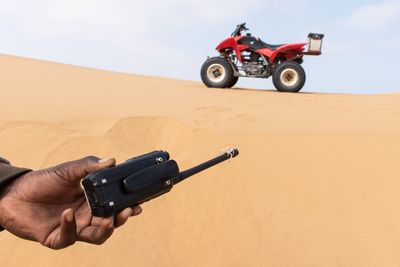 Cropped hand holding walkie-talkie near quadbike at desert