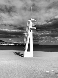 Lifeguard tower on field by sea against sky