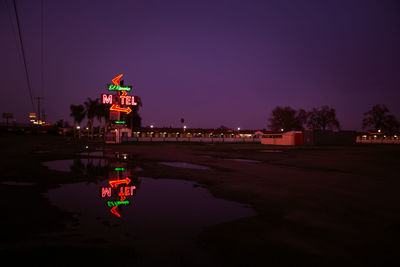 Illuminated building by street against sky at night