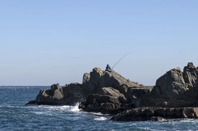 Rock formations by sea against clear blue sky