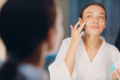 Young woman applying moisturizer on face