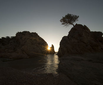 Rock formations in sea against clear sky during sunset