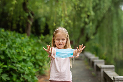 Portrait of smiling girl holding mask while standing outdoors