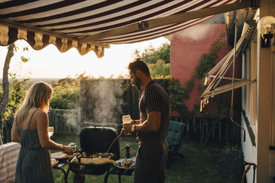 Male and female friends grilling food while having wine in party