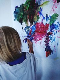 Rear view of girl painting while standing against wall