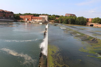 View of buildings by river against sky