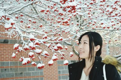Smiling young woman looking at snow covered berries at yard