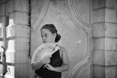 Little girl posing with folding fan against building