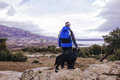 Rear view of man standing with dog on rock