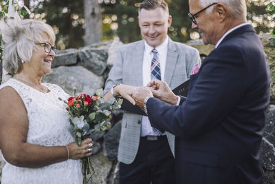 Senior groom putting wedding ring in bride's finger by minister during ceremony