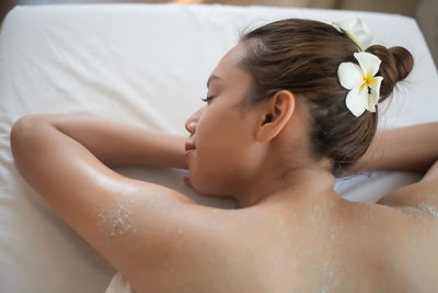 Rear view of shirtless young woman lying on massage table in spa