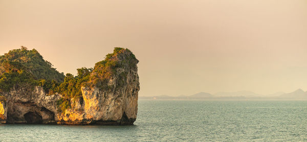 Rock formation in sea against sky during sunset