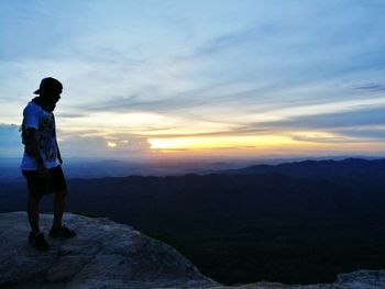 Full length of man standing on mountain against cloudy sky during sunset