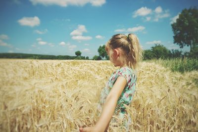 Side view of girl standing in wheat field against sky