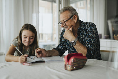 Smiling senior man helping granddaughter with homework at home
