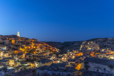 Illuminated buildings in city against clear blue sky