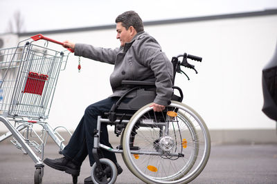 Physical disabled person in a wheelchair pushing shopping cart