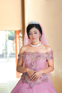 Beautiful young bride wearing wedding dress while standing at home